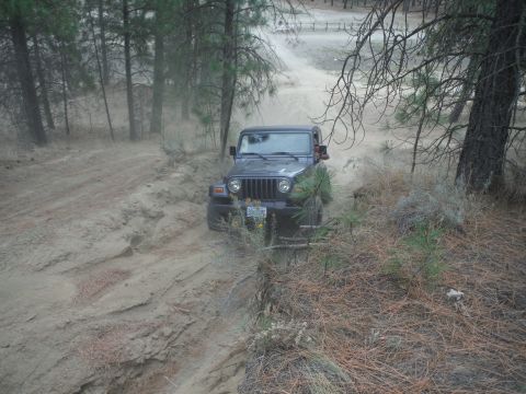 2005 Jeep Wrangler - A dark gray Jeep Wrangler navigates a dusty, off-road trail through a wooded area.