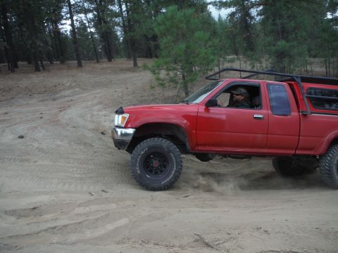 2005 Jeep Wrangler - A red pickup truck navigates a sandy, wooded terrain.