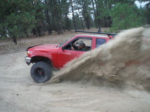 2005 Jeep Wrangler - A red pickup truck navigates a sandy terrain, generating a significant plume of dust.