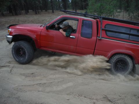 2005 Jeep Wrangler - A red pickup truck navigates a sandy trail, kicking up a cloud of dust as it goes.