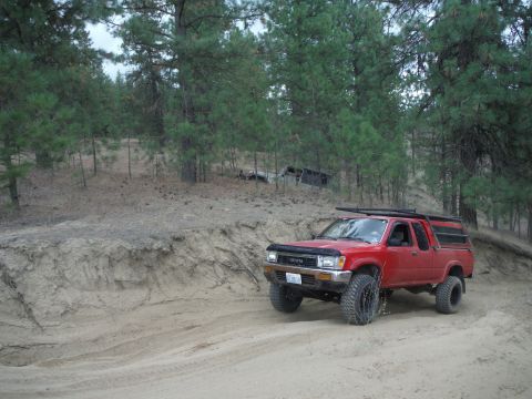 2005 Jeep Wrangler - A red Toyota pickup truck navigates a dirt path in a wooded area, with another vehicle visible in the background.