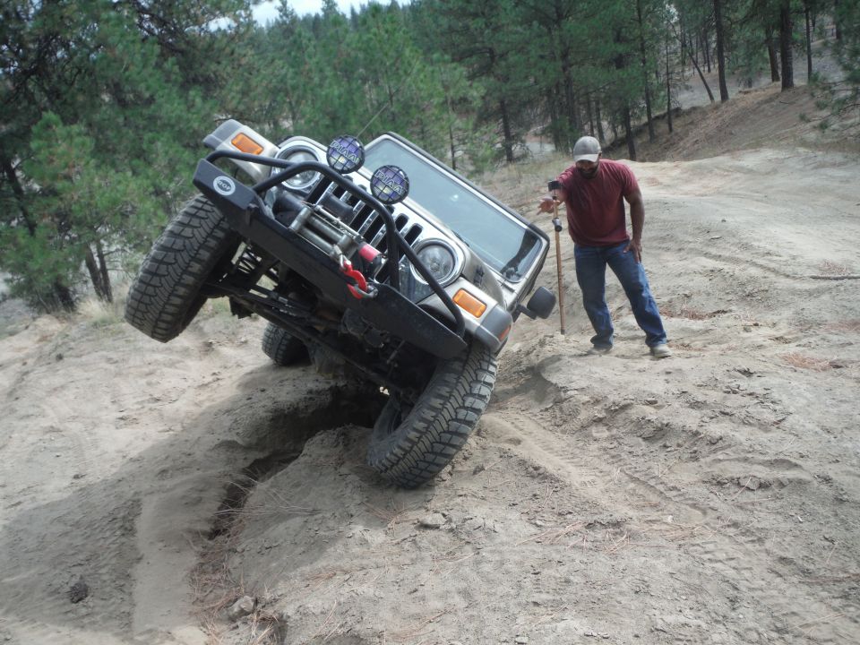 Jeep Wrangler tilted on a dirt hill with a guy standing nearby