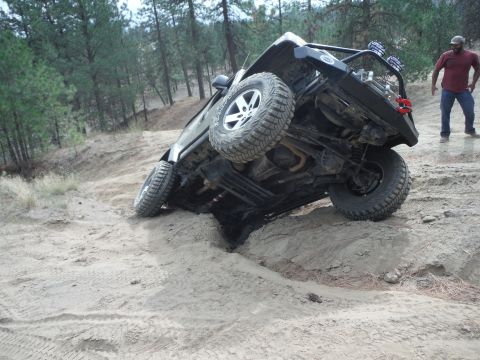 2005 Jeep Wrangler - A Jeep Wrangler is stuck on its side in a sandy off-road terrain, with a person observing the situation.