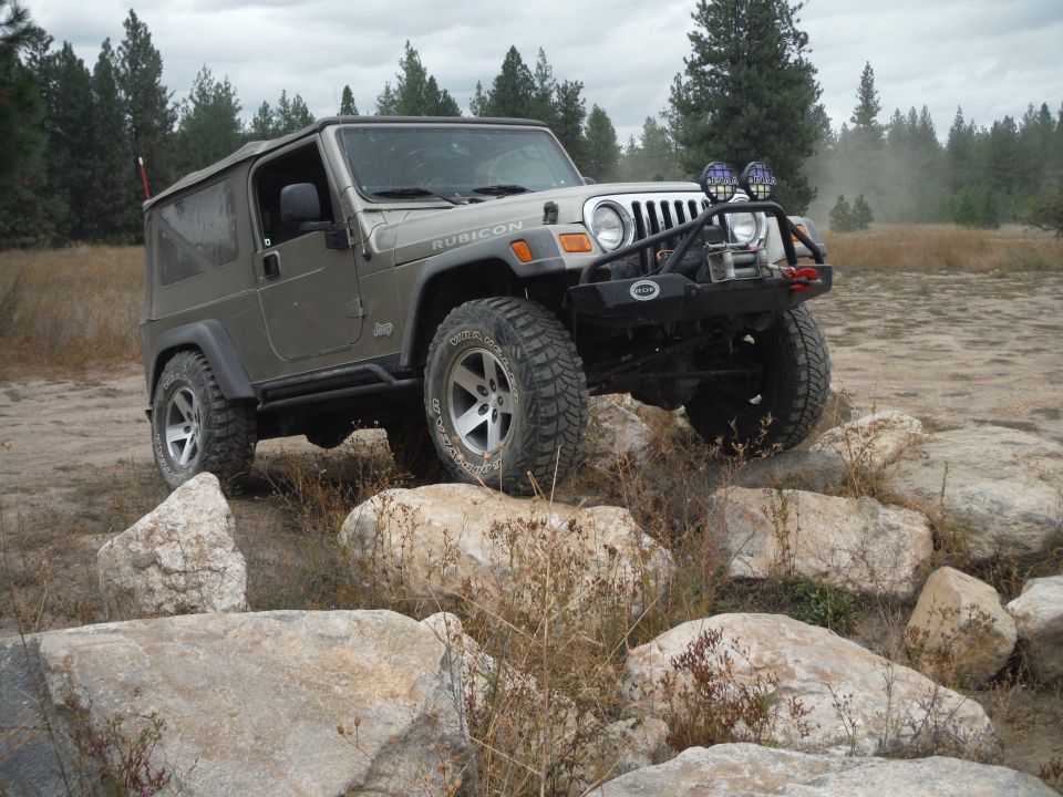 2005 Jeep Wrangler Rubicon driving over large rocks on a dirt trail
