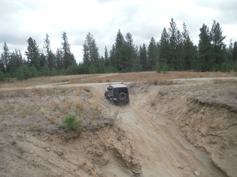 2005 Jeep Wrangler - A Jeep Wrangler navigates a steep dirt incline in a wooded, off-road environment.