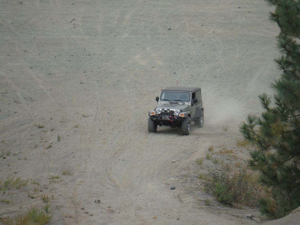 Silver Jeep Wrangler driving on a dirt road, kicking up dust. It has a winch and auxiliary lights on the front bumper