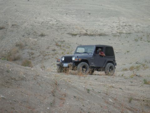 2005 Jeep Wrangler - A dark blue Jeep Wrangler navigates a dusty, off-road terrain.