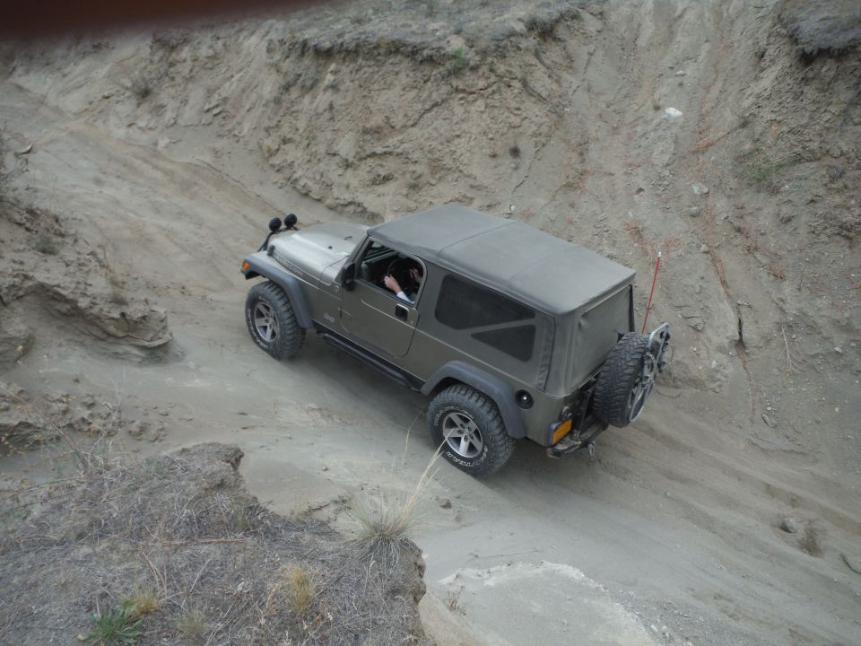 Olive green Jeep Wrangler driving down a dirt trail on a hillside