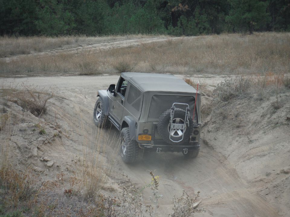 Olive green 2005 Jeep Wrangler driving on a dirt trail, rear view