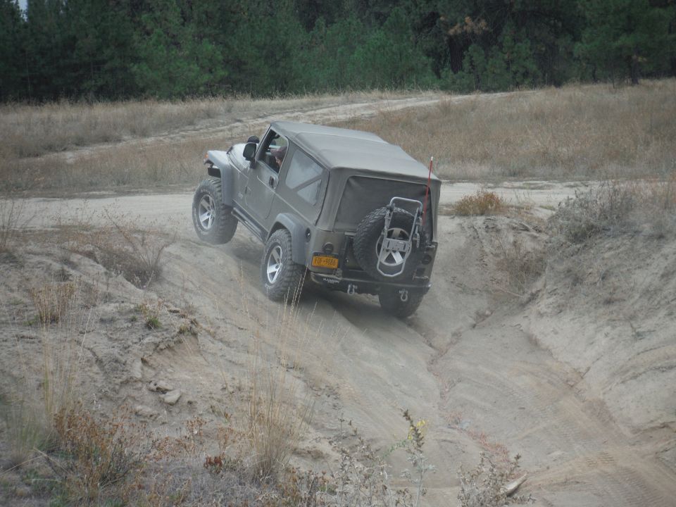 Olive green 2005 Jeep Wrangler climbing a dirt hill, rear view