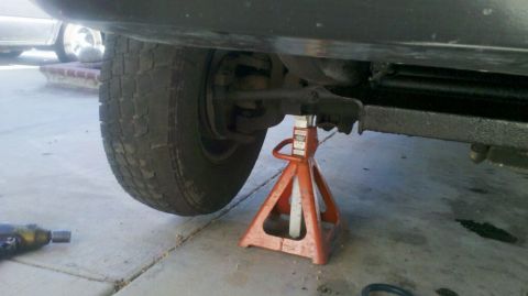 1997 Dodge 3500 - A truck's front wheel is supported by an orange jack stand, revealing the underside of the chassis and suspension.