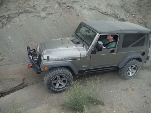 2005 Jeep Wrangler - A Jeep Wrangler Rubicon navigates a dusty, off-road path with a driver behind the wheel.
