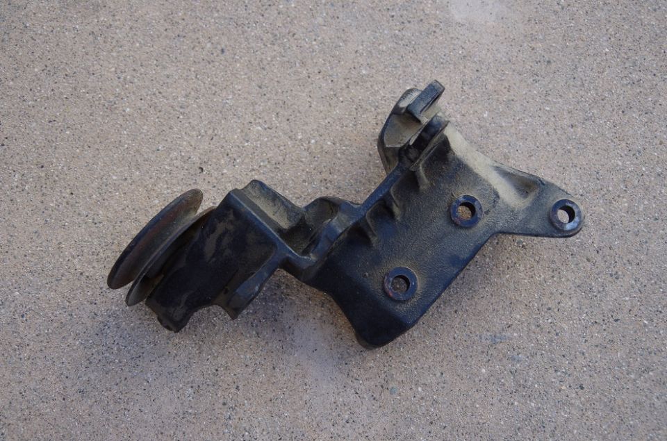 Black metal bracket with a pulley wheel attached, resting on a concrete surface