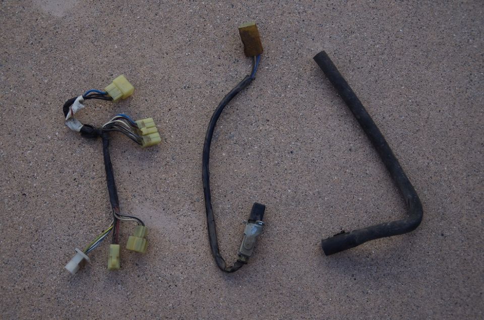 Wire harness with yellow connectors, a sensor with a black connector, and a bent black hose on a textured surface