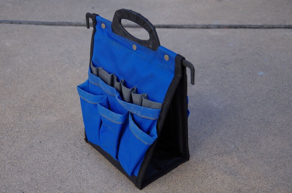 Blue fabric tool bag with multiple pockets and a black handle, sitting on concrete