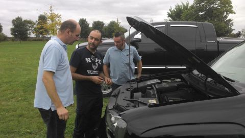 1991 Ford LTD Crown Victoria - Men inspect the engine compartment of a black vehicle, with a pickup truck visible in the background.
