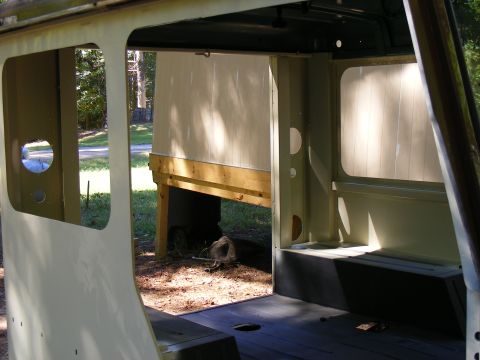 Interior view of a vehicle with exposed metal framing and unfinished panels. Wood supports are visible outside