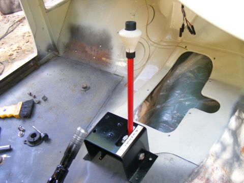 Vehicle interior showing a red gear shifter with a white knob, black base, and visible text on the base