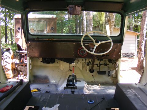 Interior view of a vintage vehicle with a white steering wheel and dashboard. Another vehicle is visible throu