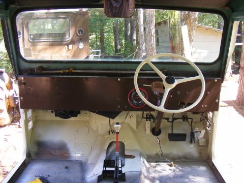 Interior view of a Jeep CJ with a white steering wheel and a red-faced gauge. Another vehicle is visible throu