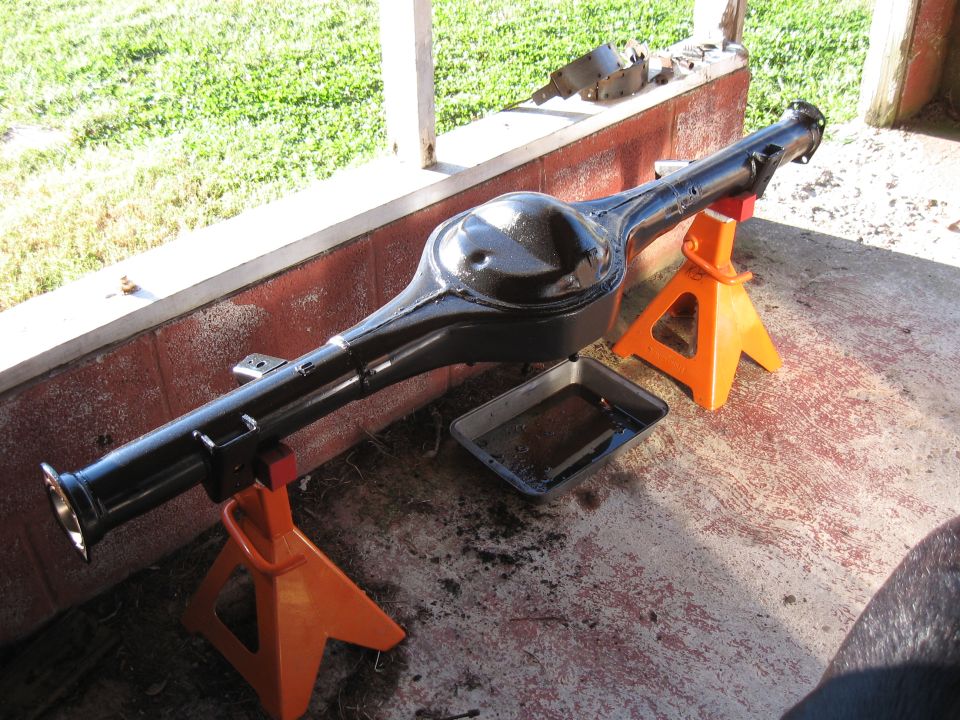 Black rear axle assembly on orange jack stands with a drip pan