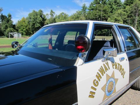 1991 Ford LTD Crown Victoria - Close-up of a black-and-white patrol car showing a red A-pillar spotlight and the gold Highway Patrol star emblem on the front door.