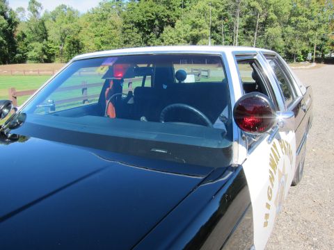 1991 Ford LTD Crown Victoria - Close-up over the hood of a black-and-white patrol car showing the windshield, interior dash and a red A-pillar spotlight.
