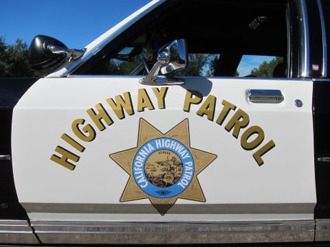 1991 Ford LTD Crown Victoria - Close-up of a black-and-white police car door painted with gold 'Highway Patrol' text and the California Highway Patrol seven-point star se…