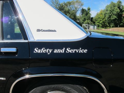1991 Ford LTD Crown Victoria - Rear quarter of a black-and-white sedan showing white 'Safety and Service' lettering and an 'LTD Crown Victoria' fender badge.
