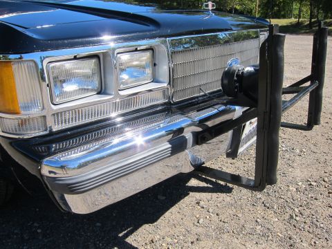 1991 Ford LTD Crown Victoria - Front-corner view of a black car showing dual headlights, an amber turn signal, chrome bumper and a mounted siren speaker behind the push b…