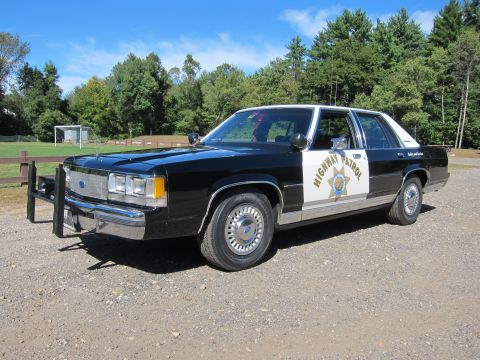 1991 Ford LTD Crown Victoria - black-and-white Ford police sedan in California Highway Patrol livery, with push bar and white door panel, parked on gravel near a field.