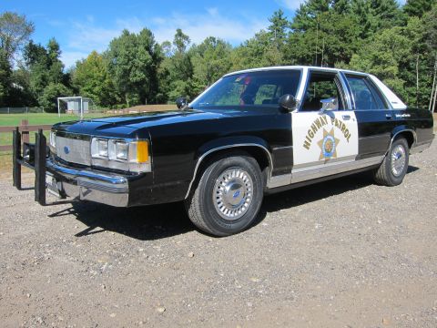 1991 Ford LTD Crown Victoria - Front three-quarter view of a black-and-white Ford police sedan in California Highway Patrol livery with a front push bar, parked on gravel.