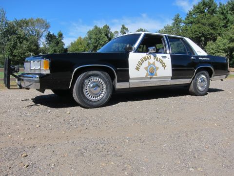 1991 Ford LTD Crown Victoria - Front three-quarter side view of a black-and-white police sedan in California Highway Patrol livery parked on gravel under blue sky.
