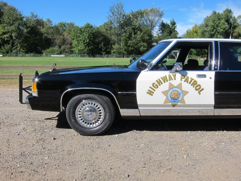 1991 Ford LTD Crown Victoria - Driver-side front section of a black-and-white police sedan with the gold California Highway Patrol star emblem on the white door panel.