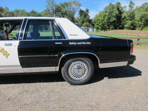 1991 Ford LTD Crown Victoria - Driver-side rear section of a black-and-white police sedan showing 'Safety and Service' lettering and an LTD Crown Victoria rear-door badge.