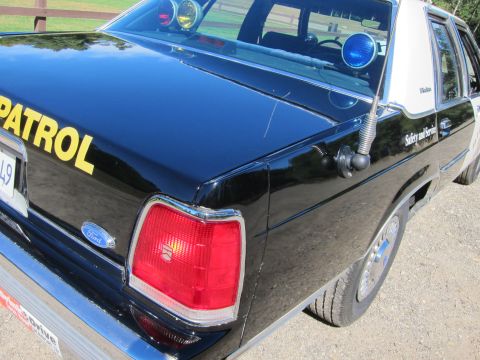 1991 Ford LTD Crown Victoria - Close-up of the rear taillight and quarter panel of a black-and-white police sedan with roof emergency lights and partial 'PATROL' letterin…