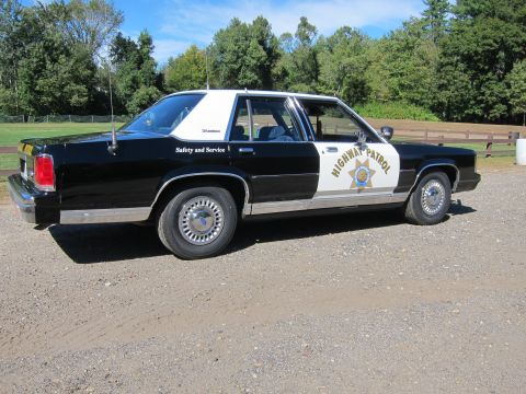 1991 Ford LTD Crown Victoria - Passenger-side rear three-quarter view of a black-and-white police sedan in California Highway Patrol livery with the gold star door emblem.