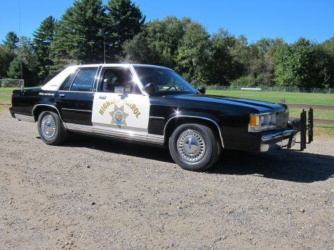 1991 Ford LTD Crown Victoria - Front-quarter view of a black-and-white California Highway Patrol sedan with a steel push bar, parked on gravel by a field.