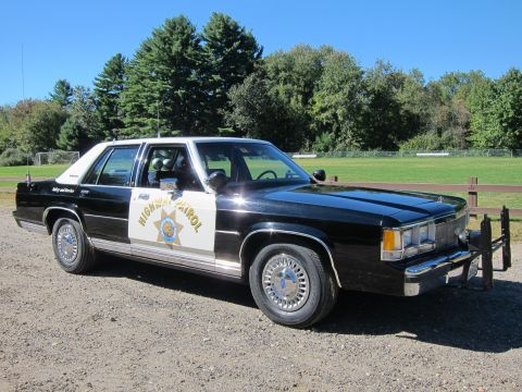 1991 Ford LTD Crown Victoria - Front three-quarter view of a black-and-white California Highway Patrol full-size Ford sedan parked on gravel by a green field.
