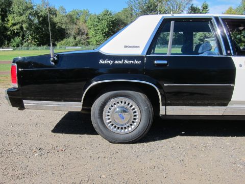 1991 Ford LTD Crown Victoria - Rear-quarter view of a black-and-white patrol sedan with 'Safety and Service' lettering and a Ford-capped wheel.