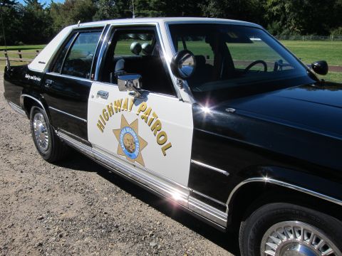 1991 Ford LTD Crown Victoria - High-angle view down the side of a black-and-white CHP sedan, gold star emblem on the white door and spotlight on the A-pillar.