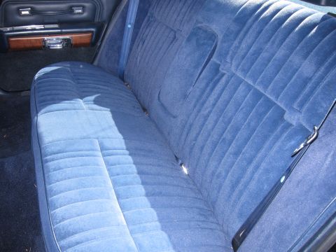 1991 Ford LTD Crown Victoria - Blue cloth rear bench seat of a full-size sedan, seatbelt draped over the cushion and woodgrain trim on the door.