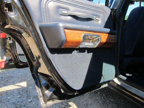 1991 Ford LTD Crown Victoria - Open blue vinyl rear door panel with woodgrain accent and chrome handle, the lower door edge over gravel.