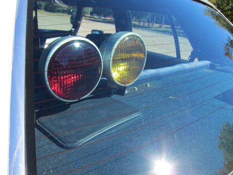 1991 Ford LTD Crown Victoria - Two round lights, one red and one amber, mounted on the rear parcel shelf and seen through the rear window of a car.