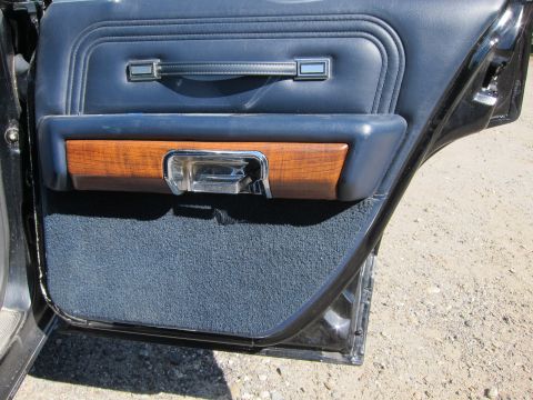 1991 Ford LTD Crown Victoria - Open blue vinyl rear door panel with woodgrain accent and chrome interior handle, parked over gravel.