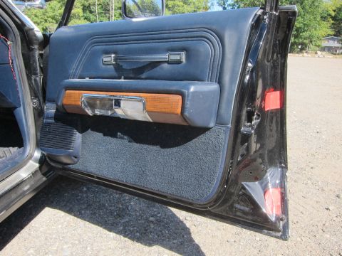 1991 Ford LTD Crown Victoria - Open blue vinyl front door panel with woodgrain accent and chrome handle, red items on the seat beyond.