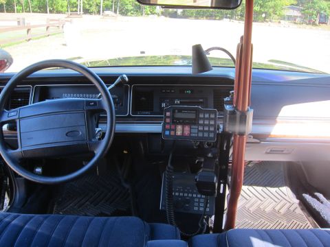 1991 Ford LTD Crown Victoria - Dashboard and front seat of a Ford sedan with a steering wheel, a center-mounted radio control head, and a handheld microphone on the floor.