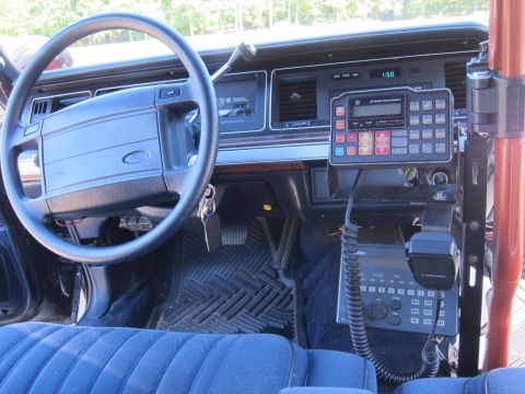 1991 Ford LTD Crown Victoria - Front dashboard of a Ford sedan with a two-way radio control head displaying 150 and a handheld microphone resting on the transmission hump.