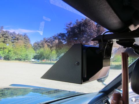 1991 Ford LTD Crown Victoria - black wedge-shaped box mounted to the inside of a car windshield, likely a radar antenna, with a sunlit field and trees visible outside.