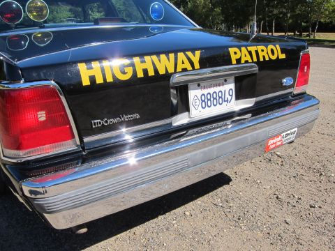 1991 Ford LTD Crown Victoria - Rear deck of a black Ford LTD Crown Victoria with yellow HIGHWAY PATROL lettering, taillights, and a California plate reading 888849.